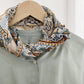 Yellow and teal paisley mulberry silk and cotton blend square neck scarf styled around the collar of a light green shirt on a hanger.