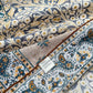 Close-up of yellow and teal paisley floral mulberry silk and cotton blend bandana square scarf showing detailed pattern and hand-rolled hem with fabric label.