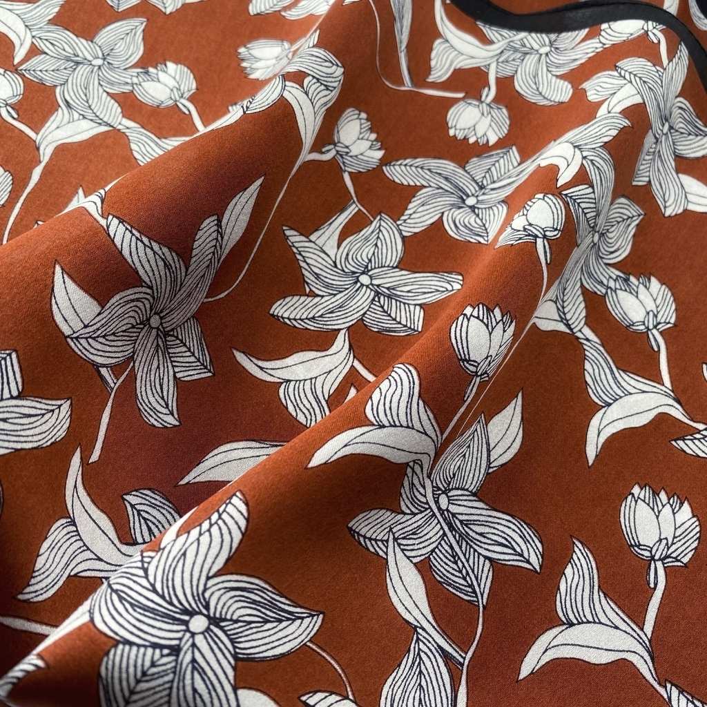 Close-up detail of a mulberry silk scarf featuring a white sketched floral pattern on a warm brown background.