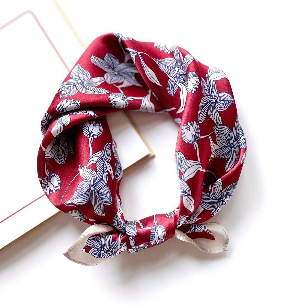 Mulberry silk square scarf with a navy and white line art floral pattern on a red background, tied into a neckerchief on a white background.