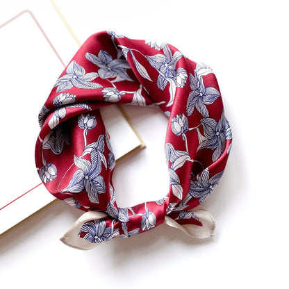 Mulberry silk square scarf with a navy and white line art floral pattern on a red background, tied into a neckerchief on a white background.