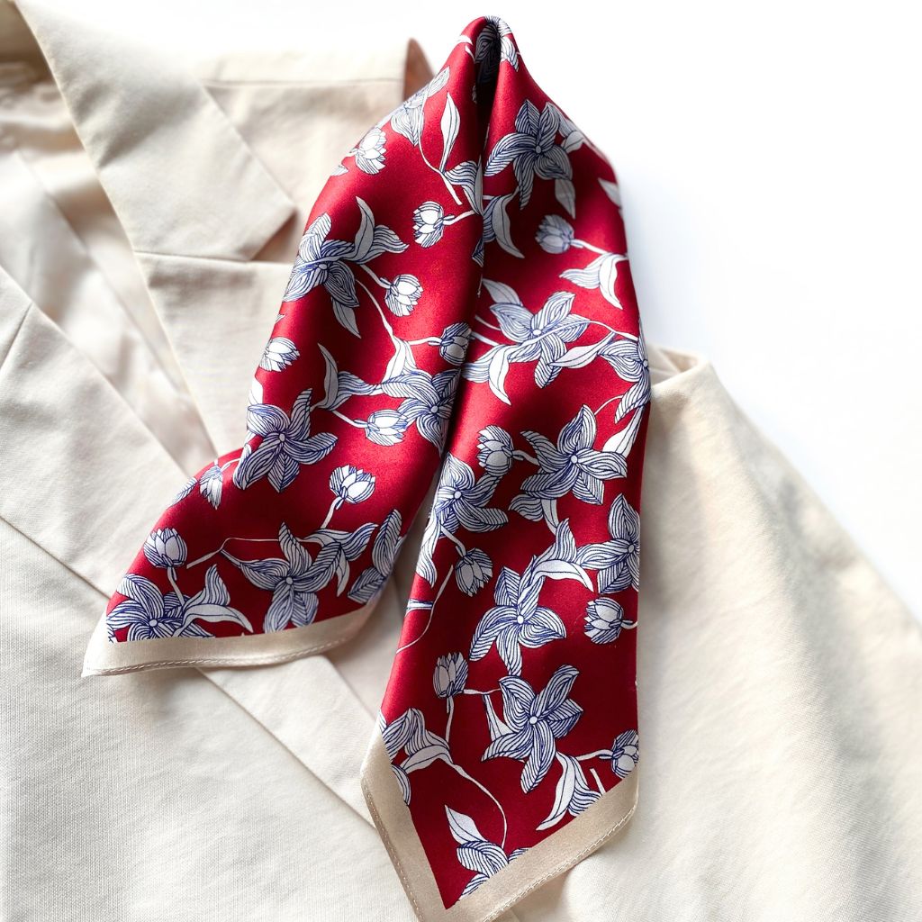 Rolled red mulberry silk square scarf with a navy and white line art floral pattern, laid on a beige top.