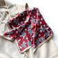 Folded mulberry silk square scarf with a navy and white line art floral pattern on a red background with a beige border, laid flat on a beige top.