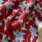 Close-up of a red silk scarf with a blue and white sketched floral pattern, featuring a cream-colored border.