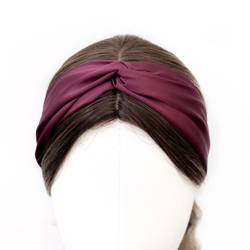 A maroon twisted mulberry silk satin headband  displayed on a brown wig mannequin head against a plain white background.