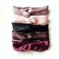 Five mulberry silk satin twisted headbands in mauve, pale pink, black, dark brown, and maroon, stacked vertically on a white background.