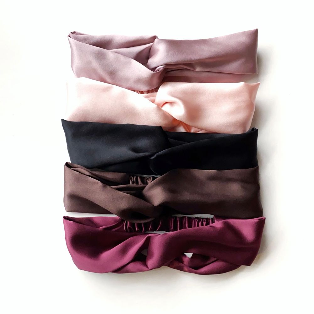 Five mulberry silk satin twisted headbands in mauve, pale pink, black, dark brown, and maroon, stacked vertically on a white background.