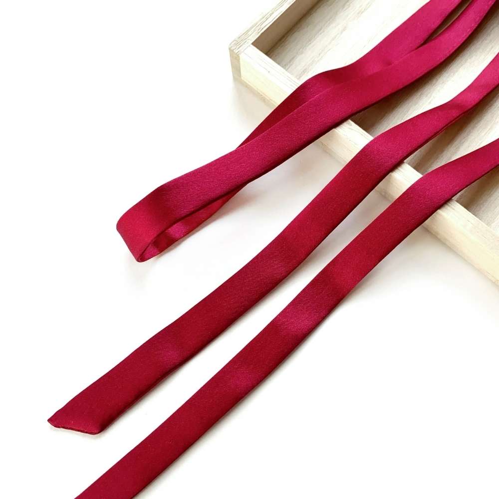 red mulberry silk skinny scarf ribbon on a white surface with a wooden box in the background.