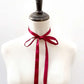 Mannequin wearing a white garment with a red silk satin ribbon neck scarf around its neck on a light gray background