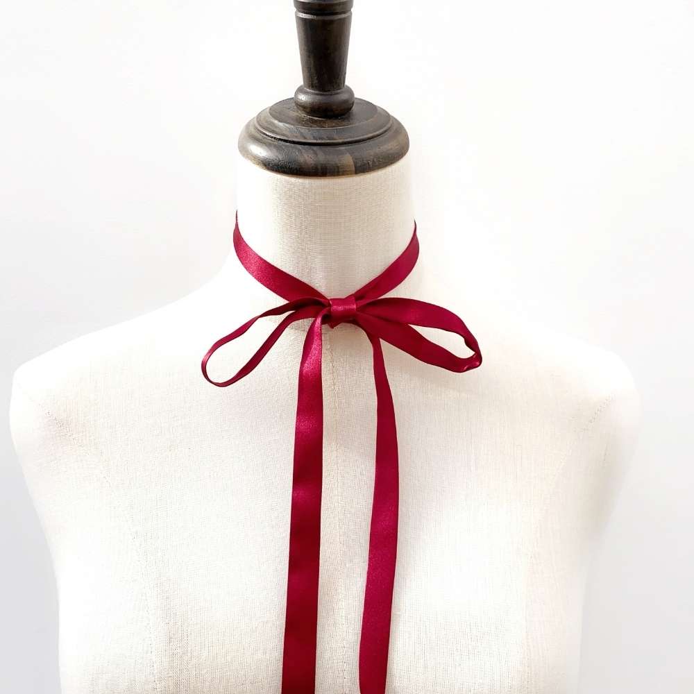 Mannequin wearing a white garment with a red silk satin ribbon neck scarf around its neck on a light gray background
