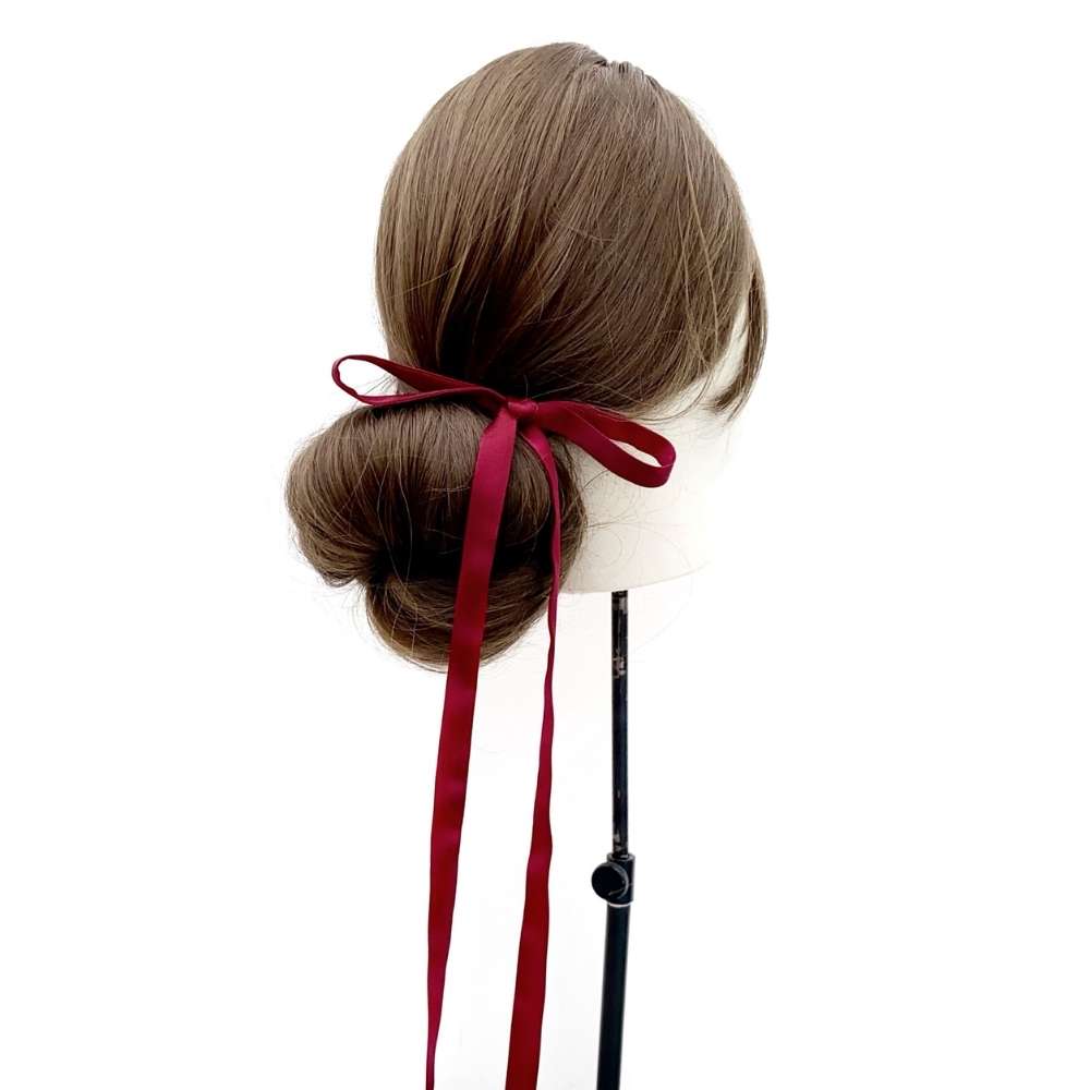 Mannequin head with brown hair styled in a bun with a red mulberry silk skinny hair tie on a white background