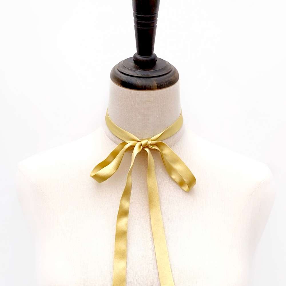 Mannequin with a Gold mulberry silk skinny ribbon scarf  tied around its neck on a white background
