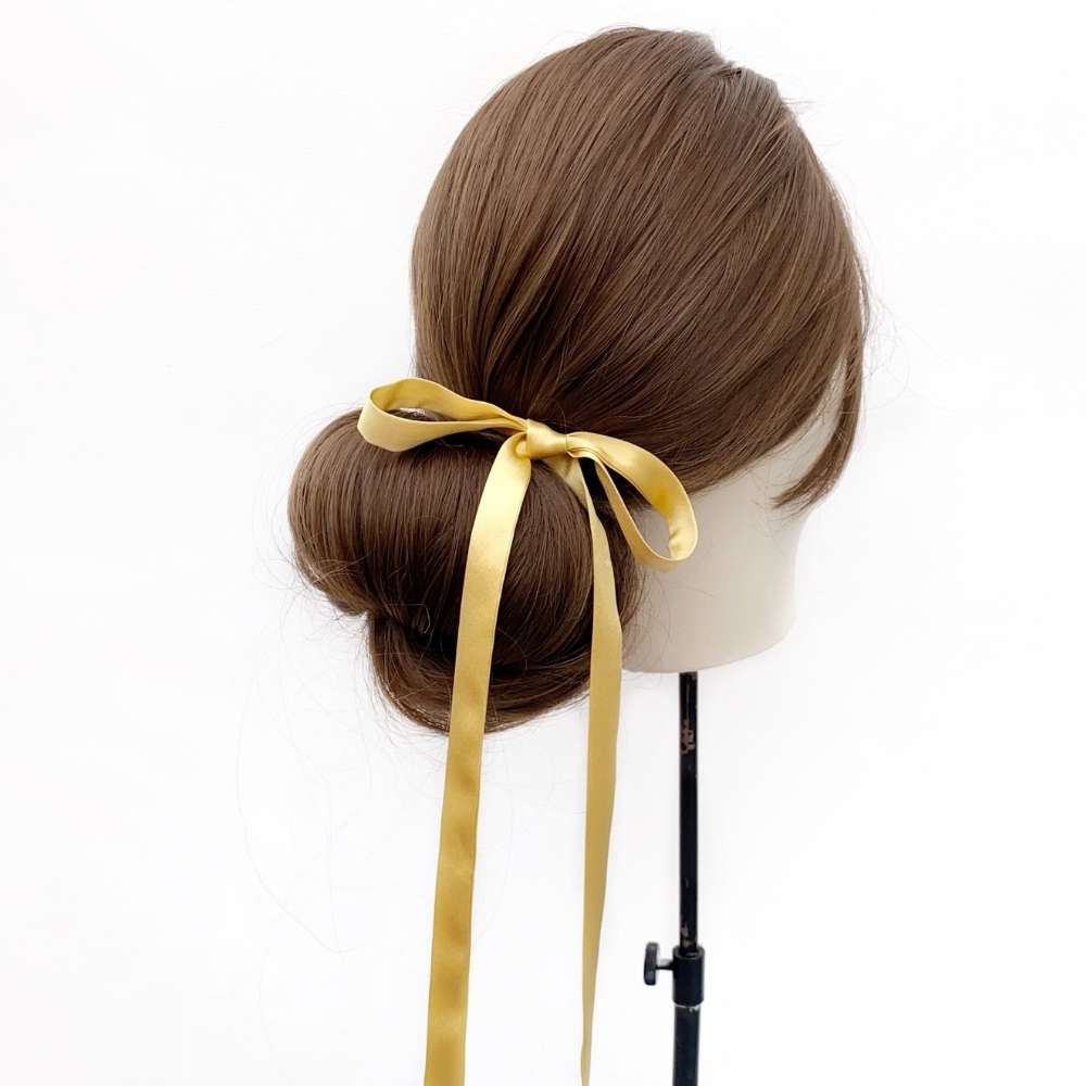 Mannequin head with brown hair styled in a bun with a Gold mulberry silk skinny ribbon hair tie on a white background
