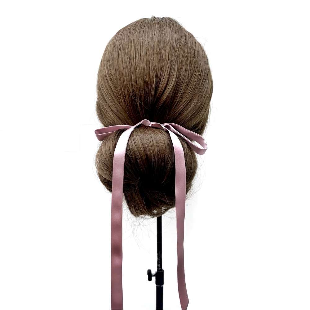 Mannequin head with brown hair styled in a bun with a muted purple mulberry silk satin ribbon hair tie on a white background