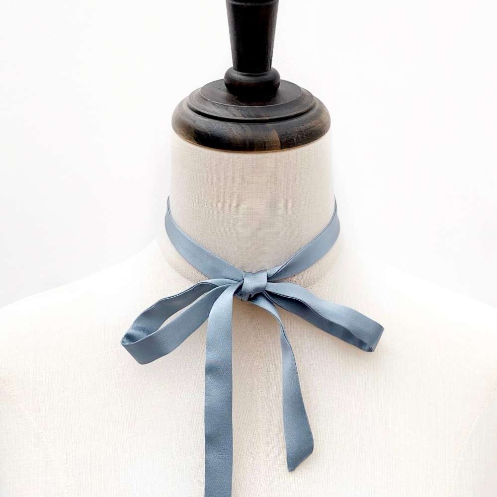 Mannequin with a dusty blue mulberry silk ribbon necktie tied around its neck on a white background