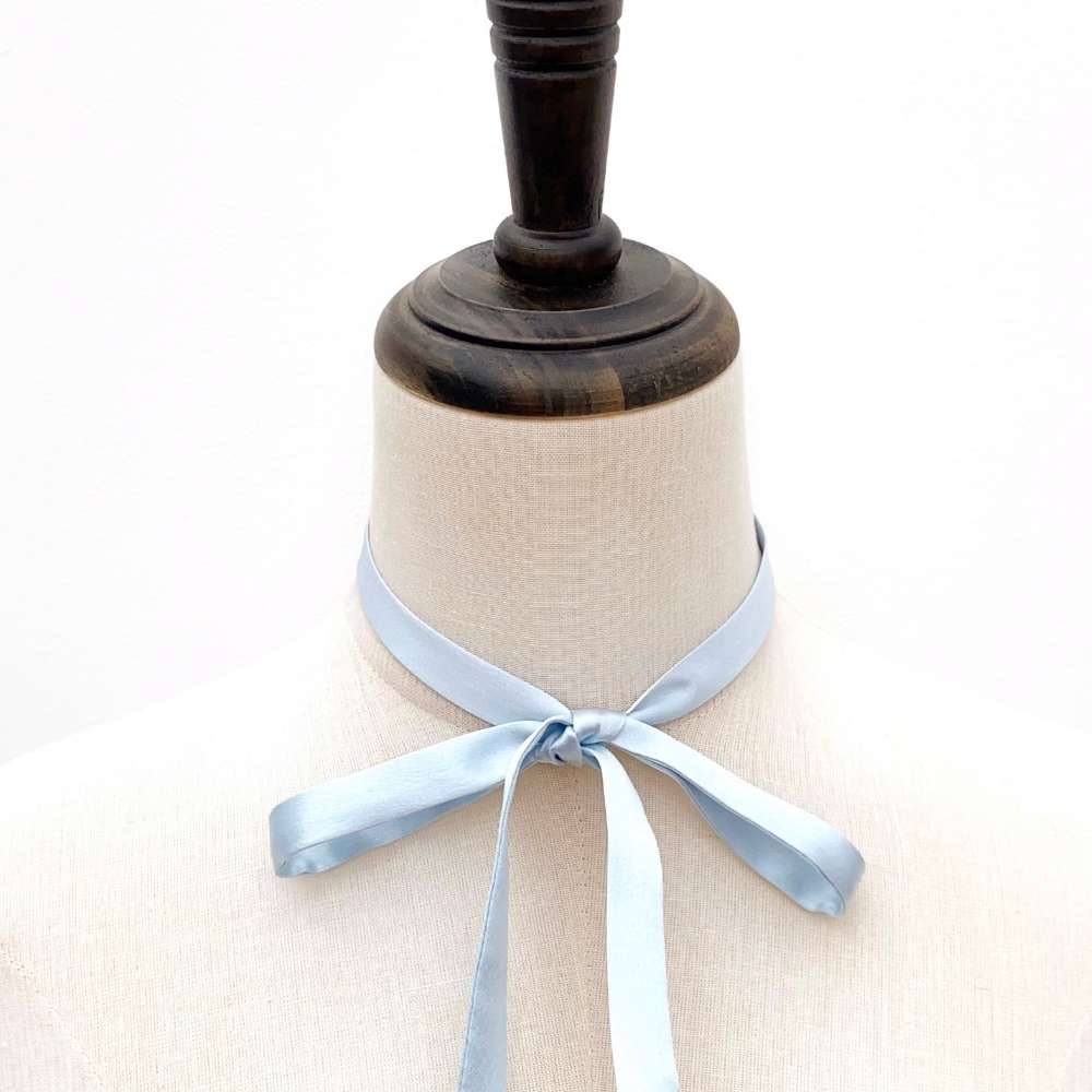 Mannequin with a light blue mulberry silk satin ribbon scarf tied around its neck on a white background