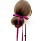 Mannequin head with brown hair styled in a bun with a purple silk hair tie ribbon on a white background