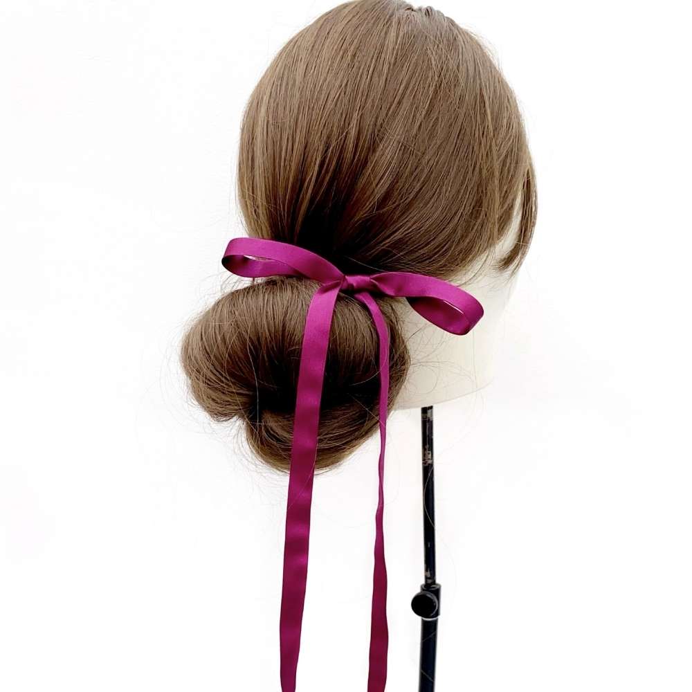 Mannequin head with brown hair styled in a bun with a purple silk hair tie ribbon on a white background