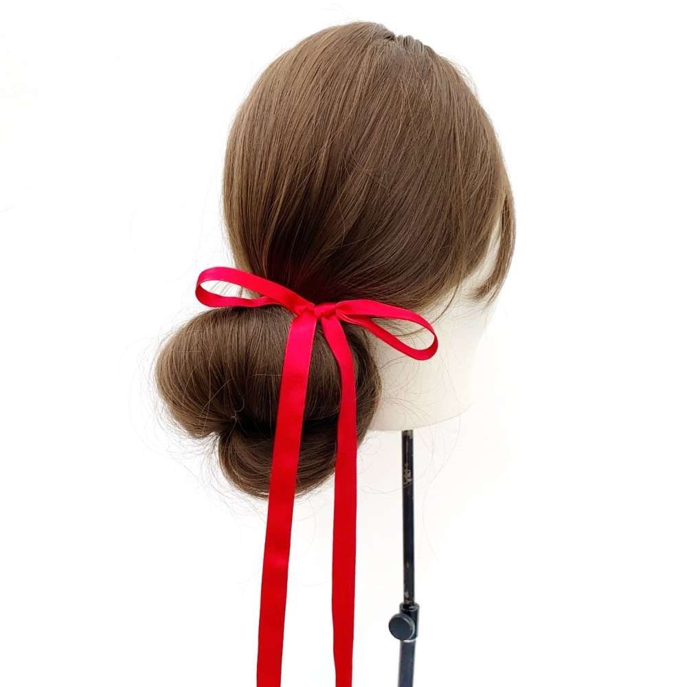 Mannequin head with brown hair styled in a bun and red silk ribbon hair tie on a white background