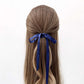 Long brown hair with a sapphire blue silk ribbon hair scarf tied in a half-up style on a white background
