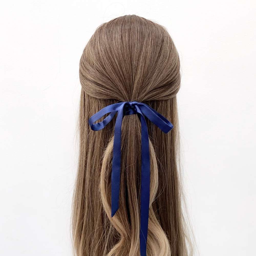 Long brown hair with a sapphire blue silk ribbon hair scarf tied in a half-up style on a white background