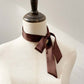 Brown mulberry silk skinny scarf tied around a mannequin neck on a plain background