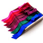 Seven mulberry silk satin scarves in a spectrum of colors including red, pink, purple, green, blue, and dark red, maroon, neatly arranged inside a light-colored wooden box on a white background.