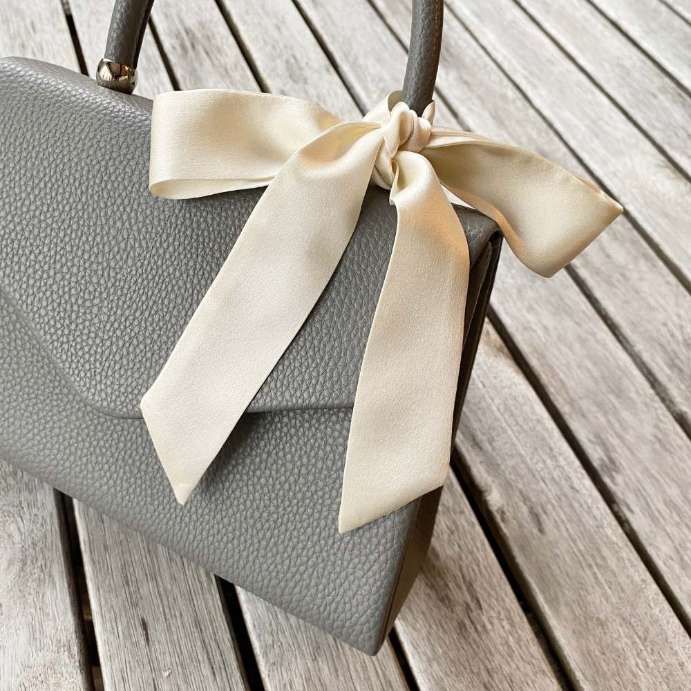 Gray handbag with a mulberry silk twilly scarf  on a wooden surface