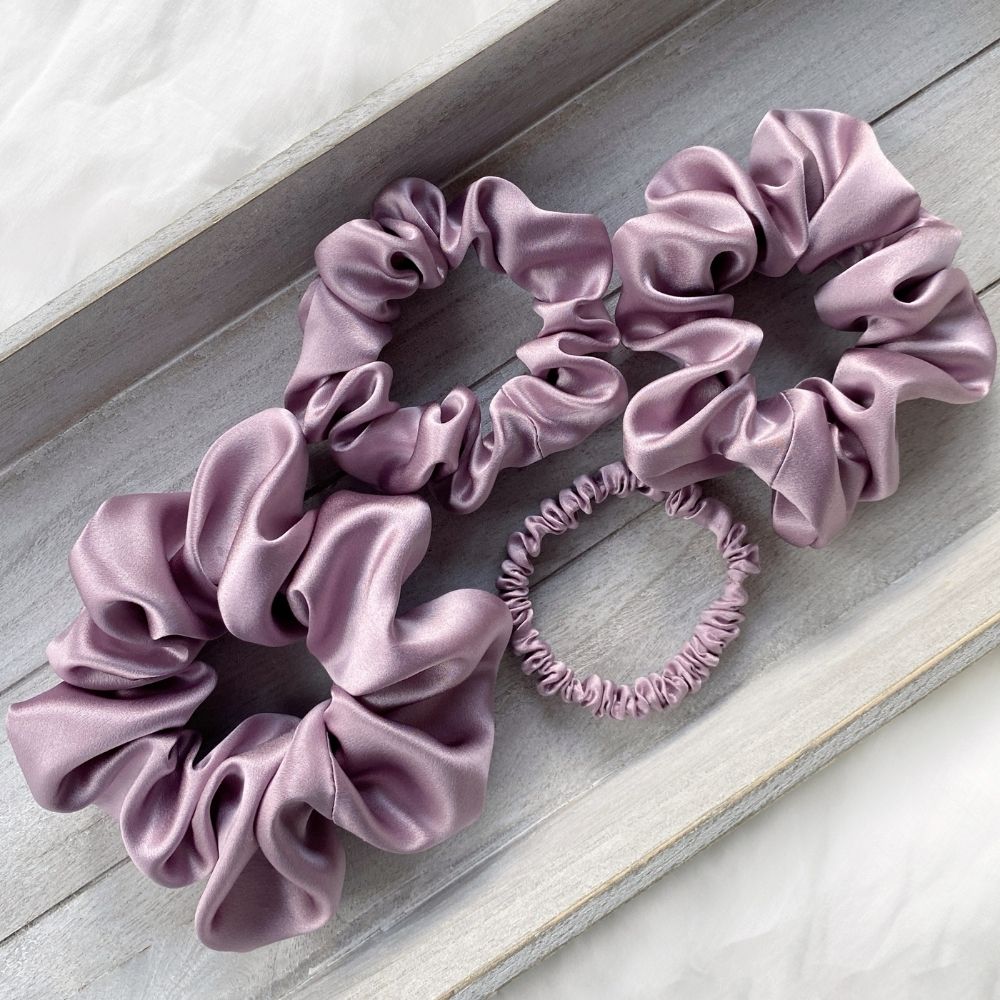 Set of purple pure mulberry silk satin scrunchies and hair ties on a wooden surface