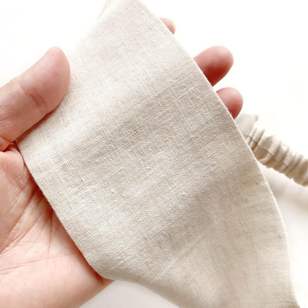 Close-up of a hand holding a natural linen fabric headband.