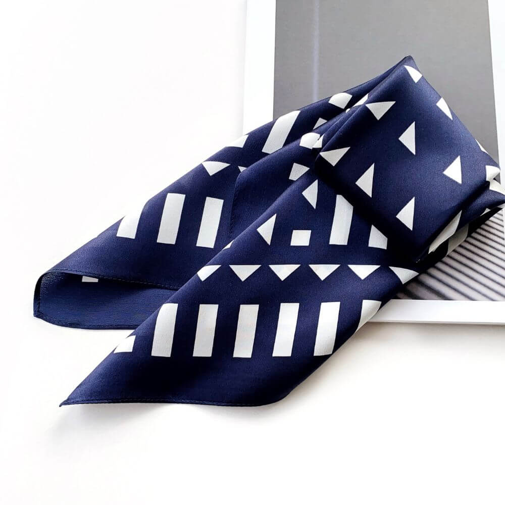 Navy blue silk scarf with white geometric pattern on a white surface