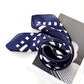 Navy blue silk scarf wrapped as a swirl with white geometric pattern on a white background