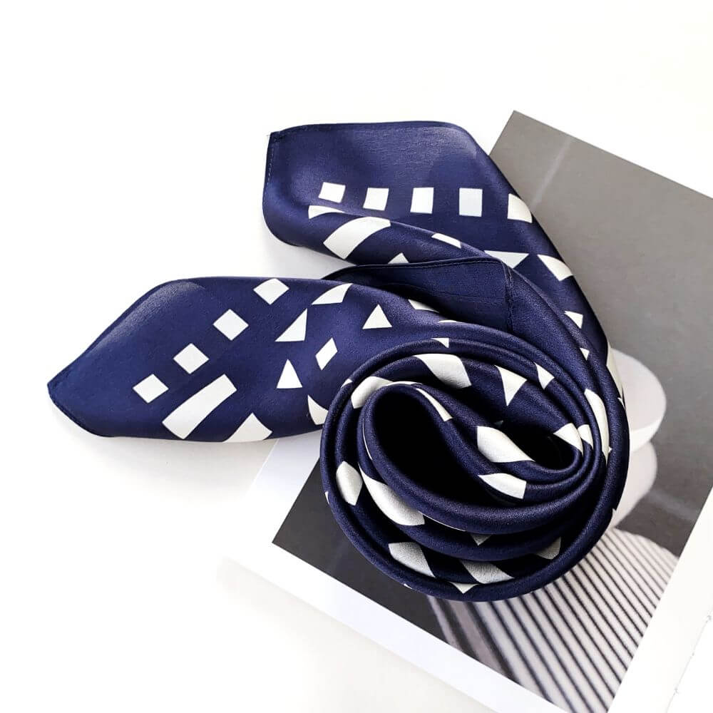 Navy blue silk scarf wrapped as a swirl with white geometric pattern on a white background