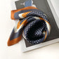 navy and brown geometric patterned mulberry silk square scarf on a magazine with a white background