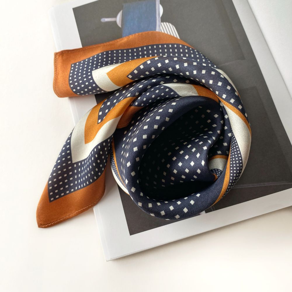 navy and brown geometric patterned mulberry silk square scarf on a magazine with a white background