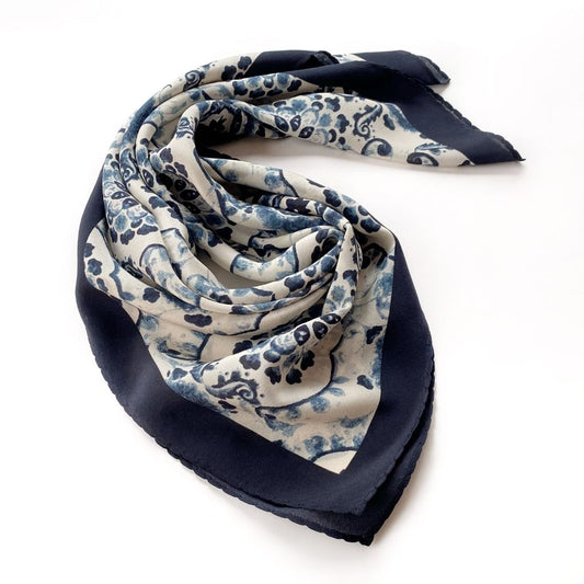 A rolled blue and white geometric floral print mulberry silk bandana scarf laid flat on a white background.