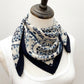 A mannequin wearing a white top and styled with a navy blue and white geometric floral print mulberry silk square scarf wrap around the neck.