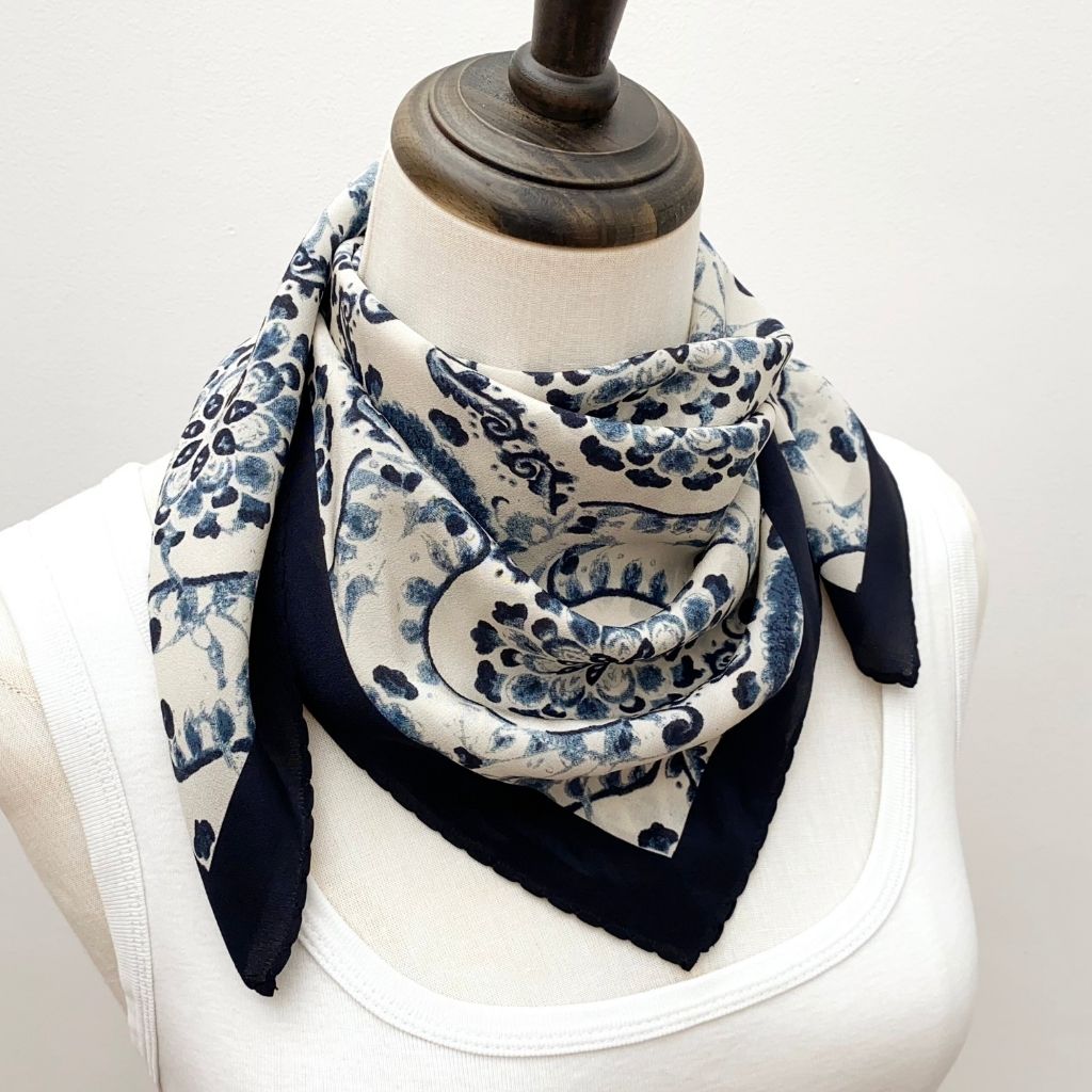 A mannequin wearing a white top and styled with a navy blue and white geometric floral print mulberry silk square scarf wrap around the neck.