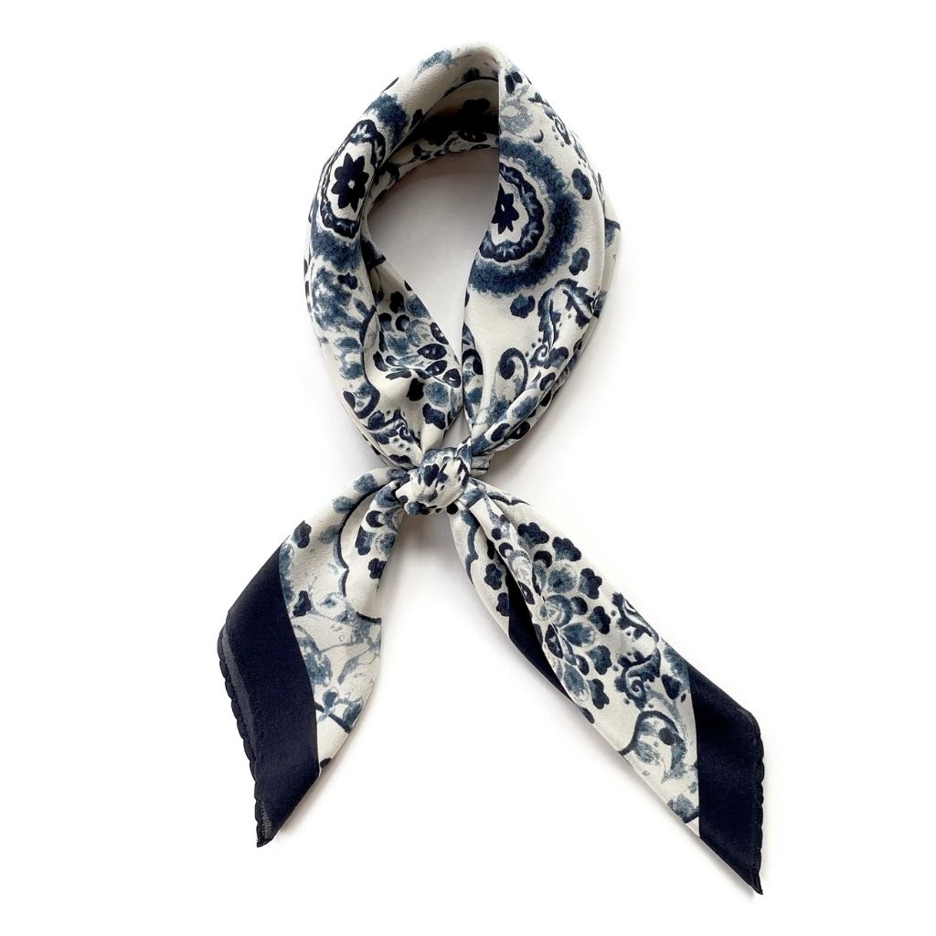 A blue and white geometric floral print mulberry silk neck scarf tied in a neat knot against a white background.