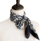 A mannequin wearing a white top with a navy blue and white geometric floral print mulberry silk neckerchief tied loosely around the neck.