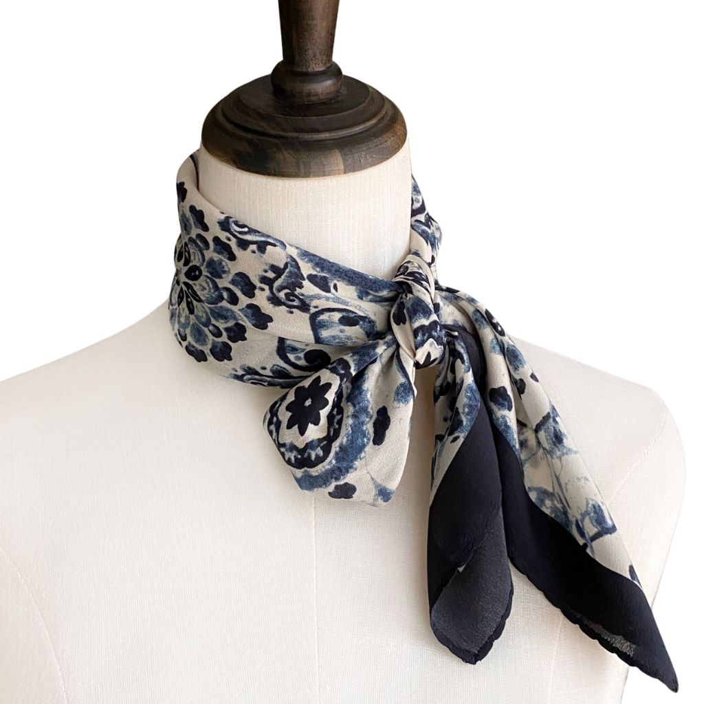 A mannequin wearing a white top with a navy blue and white geometric floral print mulberry silk neckerchief tied loosely around the neck.