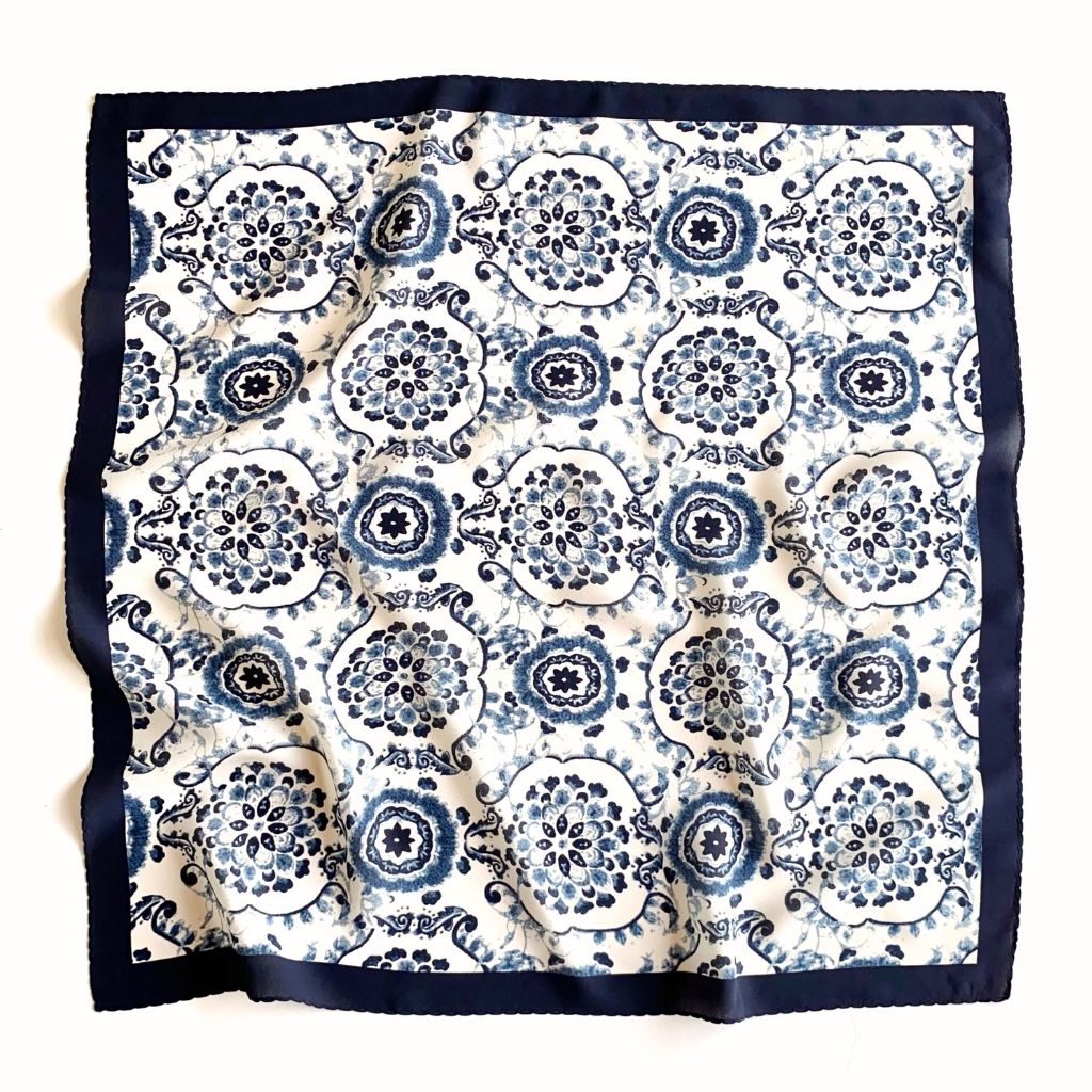 A full view of a square mulberry silk scarf featuring a blue and white geometric floral pattern with a solid navy border, laid flat on a white background.