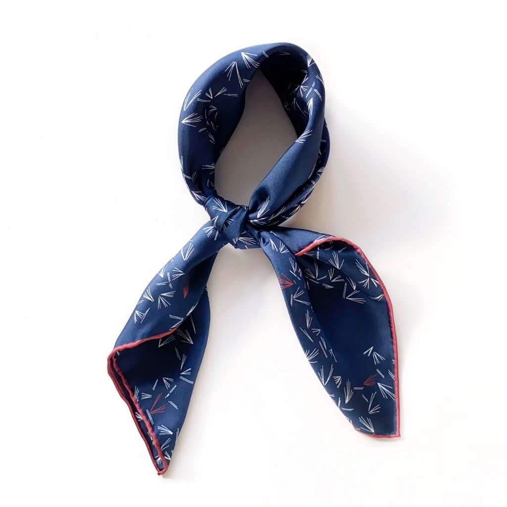 Tied navy blue mulberry silk neck scarf with white abstract patterns and contrasting red border.
