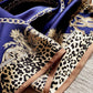 A close-up of a luxury mulberry silk scarf featuring a deep blue background with gold chain and baroque motifs, a beige leopard print section, and a contrast border.