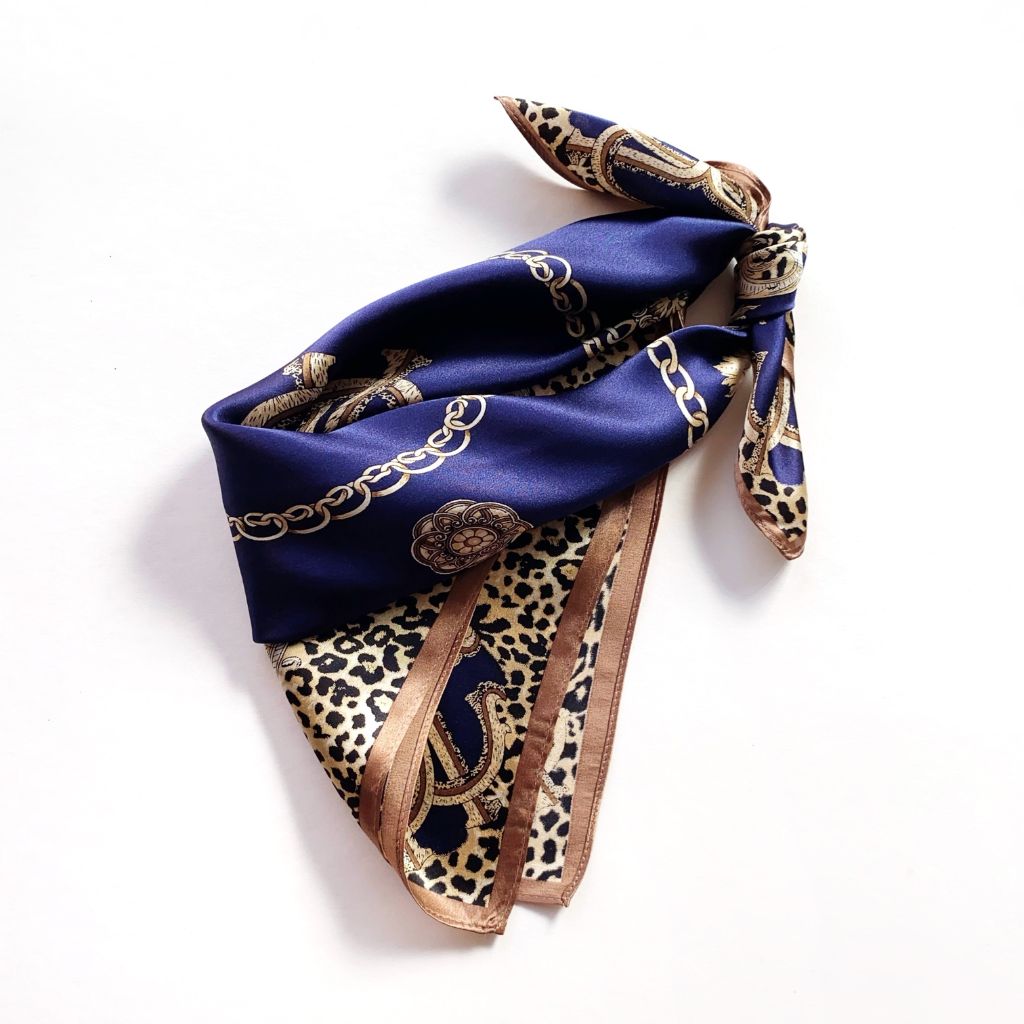 A folded mulberry silk square scarf featuring a navy blue center with gold chain motifs and a leopard print section on a white background.