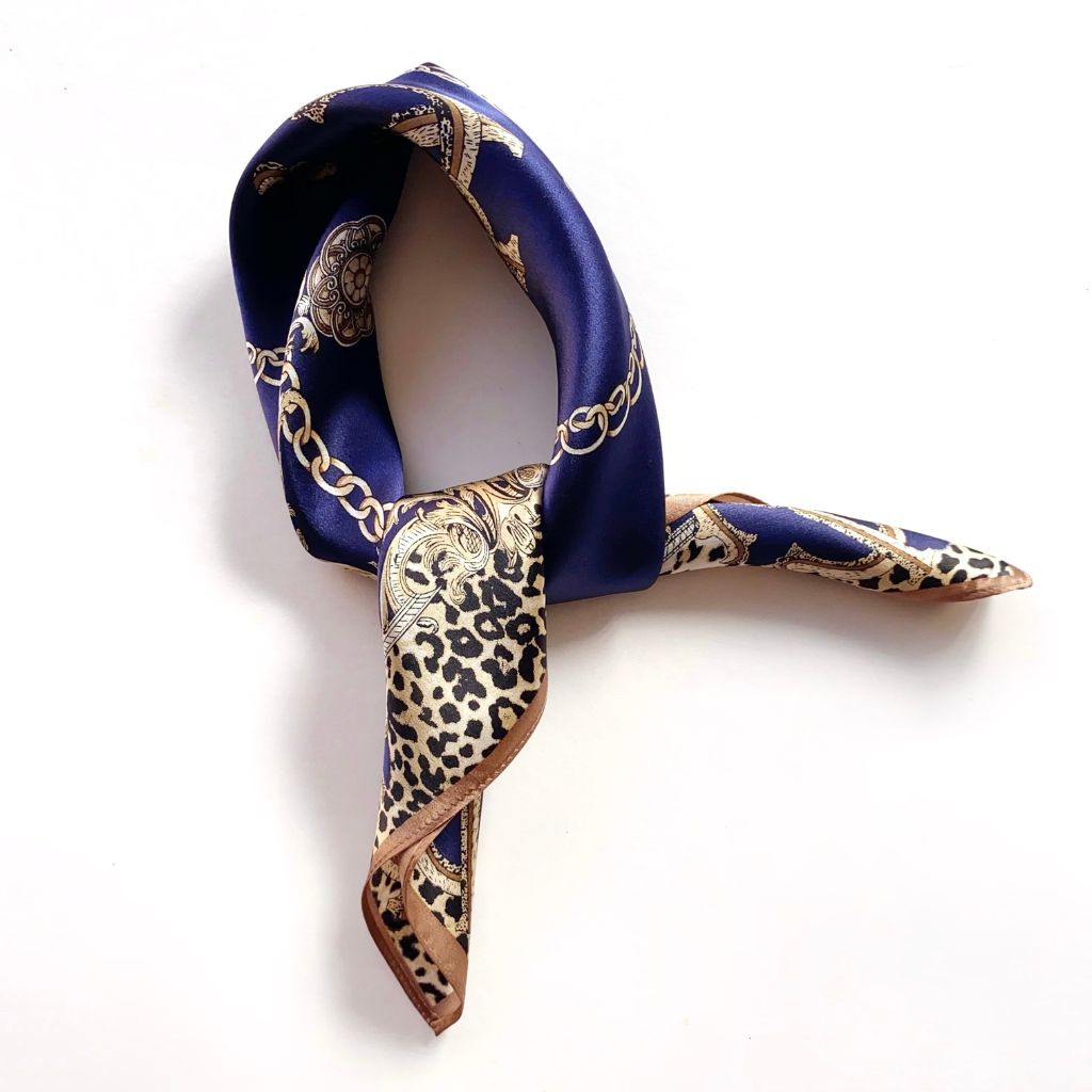 A mulberry silk scarf with a navy blue and beige chain-link pattern and a leopard print section, styled in a knot on a white background.