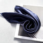 A dark navy blue mulberry silk scarf elegantly draped over a modern art print on a textured gray surface.
