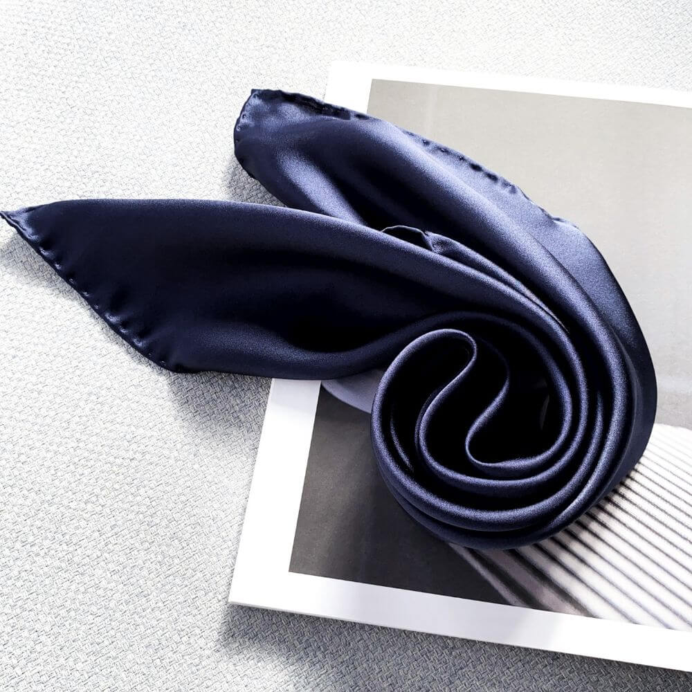 A dark navy blue mulberry silk scarf elegantly draped over a modern art print on a textured gray surface.