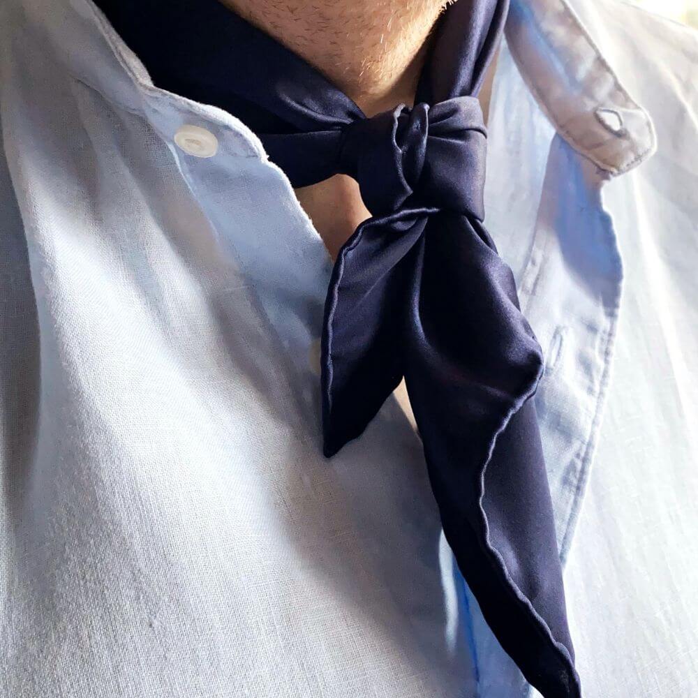 Navy blue mulberry silk scarf tied around a person's neck with a light blue shirt.
