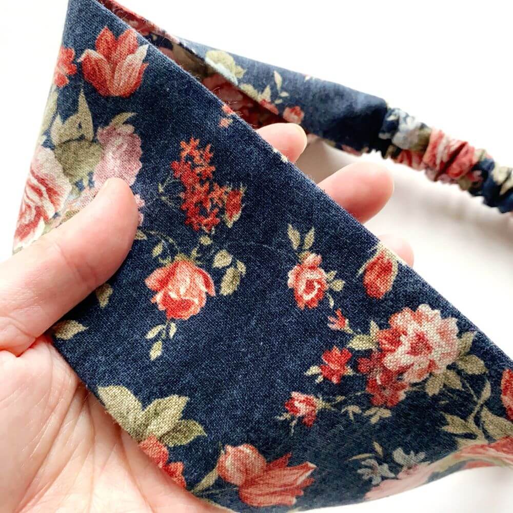 navy rose floral-patterned headband held by a hand with a white background